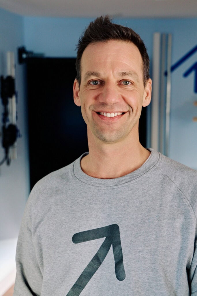 Motivationscoach im Studio, lächelnd, in casual Kleidung, positive Atmosphäre.