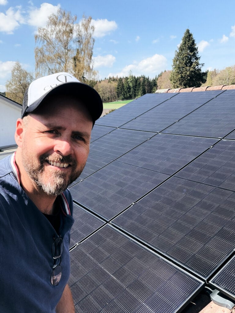 Mann vor Solaranlage auf Hausdach in Söcking bei Sonnenschein.