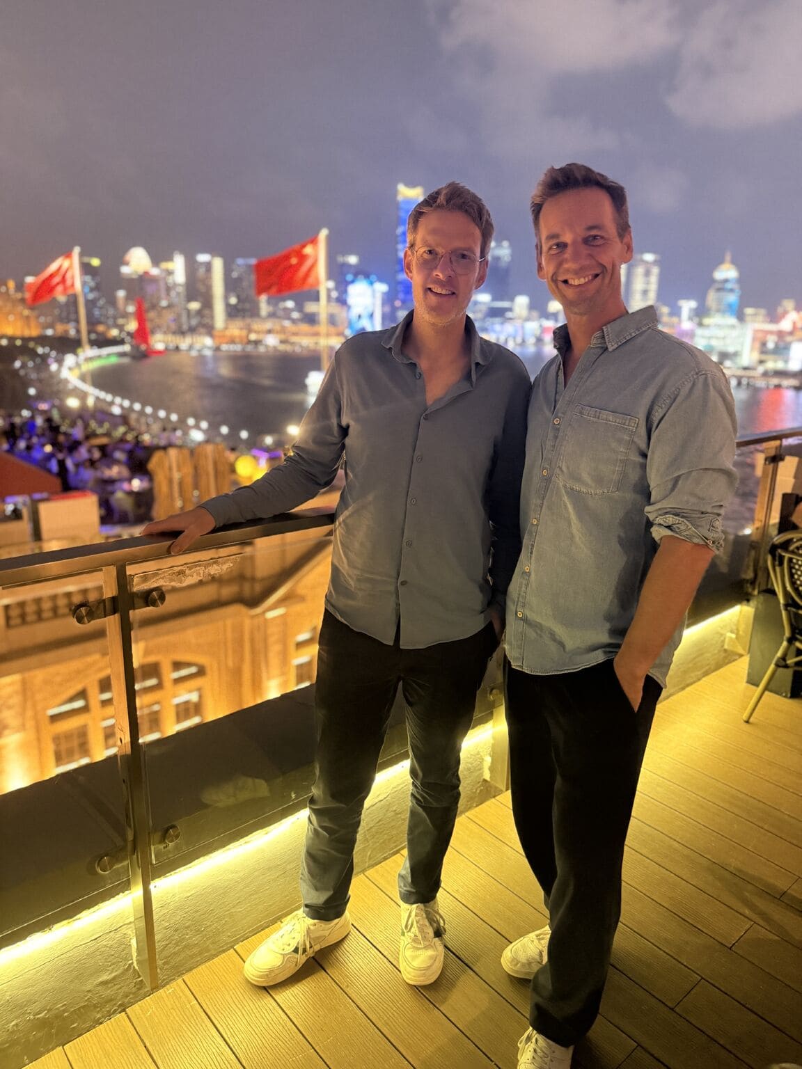 Zwei Männer auf einer Dachterrasse mit Blick auf die Skyline bei Nacht.